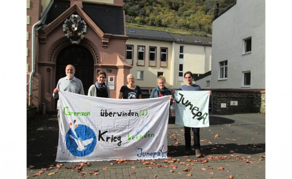 Die genannten Personen halten ein Transparent mit der Aufschrift "Grenzen überwinden(d) Krieg beenden"