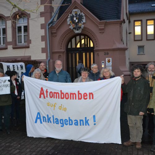 Eine Gruppe winterlich angezogener Menschen hält ein weißes Transparent mit der genannten Aufschrift in rot, gelb und blau vor sich. Im Hintergrund die schöne Fassade aus rotem Sandstein und hellem Putz des Amtsgerichts Cochem. Draußen ist es dämmrig; aus den Fenstern fällt Licht.