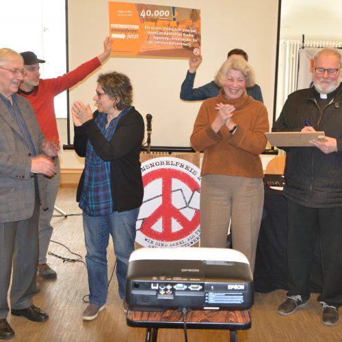Die Personen haben offensichtlich gute Laune, klatschen sich Beifall. Im Hintergrund heben zwei ein Schild in die Höhe, auf dem zu lesen ist "die 40.000ste Unterschrift unter den Appell an die künftige Bundesregierung "Unterzeichnen Sie den Atomwaffenverbotsvertrag!"