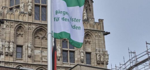 Eine grün-weiße Flagge weht vor einem gotischen Turm.