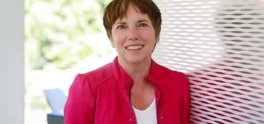 Eine Dame mit kurzen dunklen Haaren in roter sportlich-schicker Jacke und weißem Shirt schaut freundlich in die Kamera.