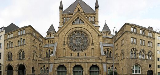 Symmetrischer prächtiger Sakralbau aus Sandstein mit zentralem Rundfenster im dreitürigen Portal und Davidstern auf dem Spitzdach.