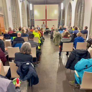 Ein voll besetzter heller Kirchenraum, an dessen Ende mehrere Vortragende sitzen.