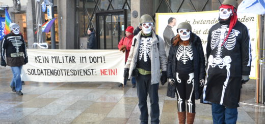 Drei als Skelette mit Soldatenhelm verkleidete Menschen vor einem Transparent.