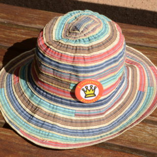 Ein bunt gestreifter Sommerhut mit einem Button "Lumpenpazifist".