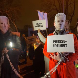 Hinter Joe Biden und Julian Assange sind weitere Leute zu sehen, die "Julian-Assange"-Schilder hochhalten
