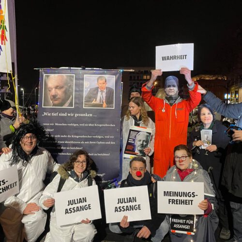 Ein knappes Dutzend gut gelaunte Aktivist*innen, als Julian Assange, Joe Biden, Annalena Baerbock, Gefangene und Clowns verkleidet, zeigen ihre Schilder und Plakate.