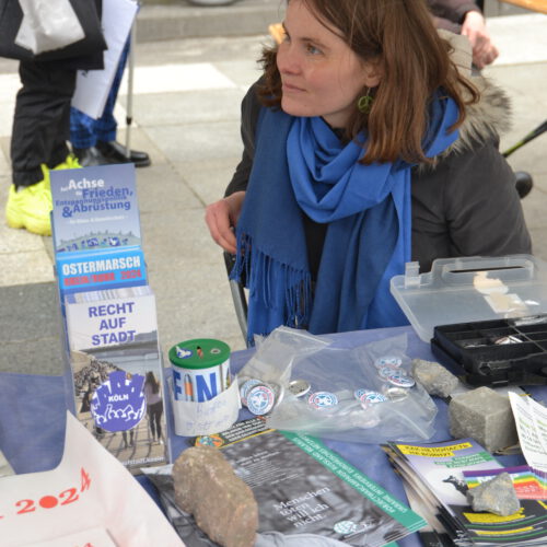 Eine junge Frau hinter einem Tisch mit Infomaterial schaut konzentriert zur Seite.