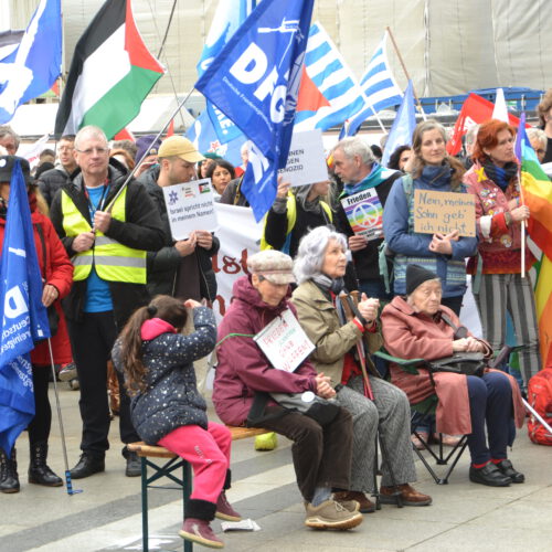 Gedrängt stehende und sitzende Leute mit Schildern und Fahnen