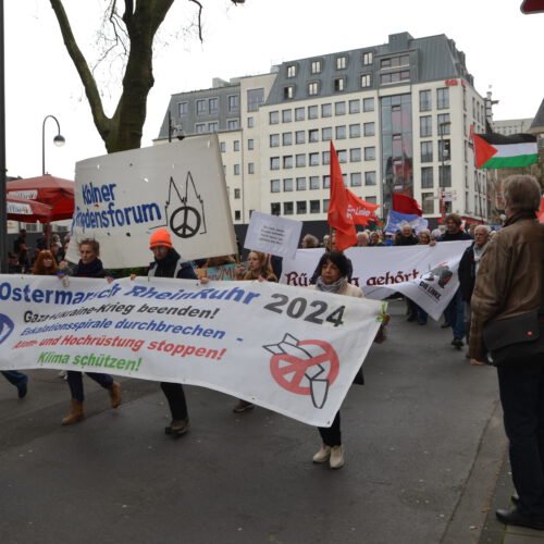 Eine Menschenmenge formiert sich hinter einem Fronttransparent "Ostermarsch Rhein Ruhr 2024"