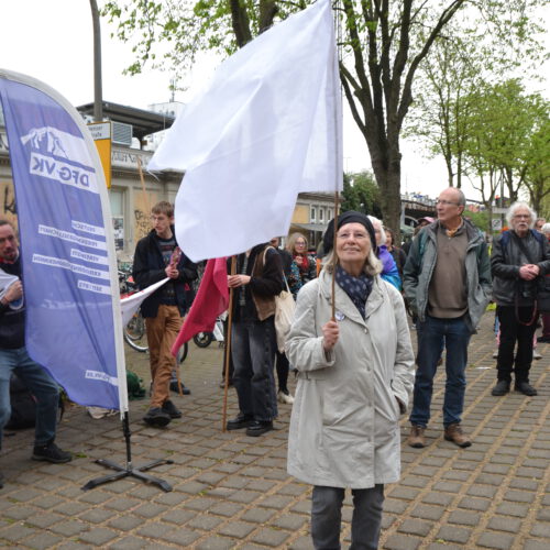 Eine fröhlich schauende ältere Dame mit einer weißen Flagge vor einer Gruppe Menschen