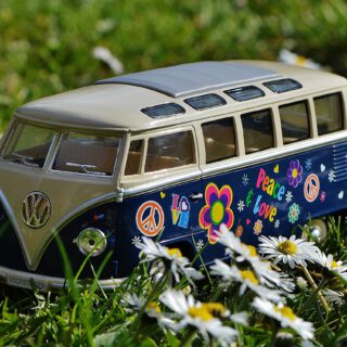 Ein mit Blumen und Peace-Zeichen bemalter Spielzeug-VW-Bulli steht auf einer Wiese zwischen Gänseblümchen.